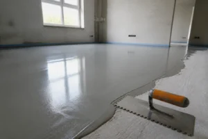 Ragréage autolissant gris frais étalé sur un sol de chantier avec une spatule posée à côté