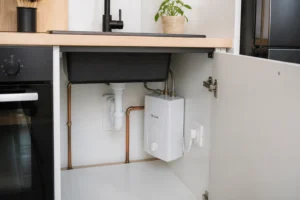 Chauffe-eau instantané électrique compact installé sous un évier de cuisine, vue rapprochée des connexions plomberie