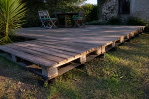 Terrasse en bois de palette dans un jardin, planches espacées sur structure surélevée