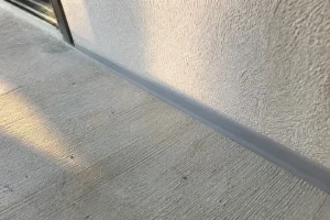 Joint de dilatation en mastic gris entre une terrasse béton et le mur d'une maison