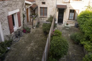 Cour commune pavée entre deux maisons mitoyennes avec clôture basse et jardin partagé