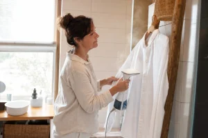 Défroisseur vapeur utilisé sur une chemise en coton suspendue dans une salle de bain